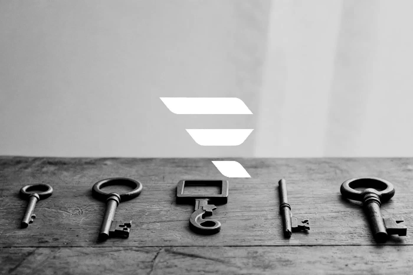 Five antique keys and a pen laid out in a row on a wooden table