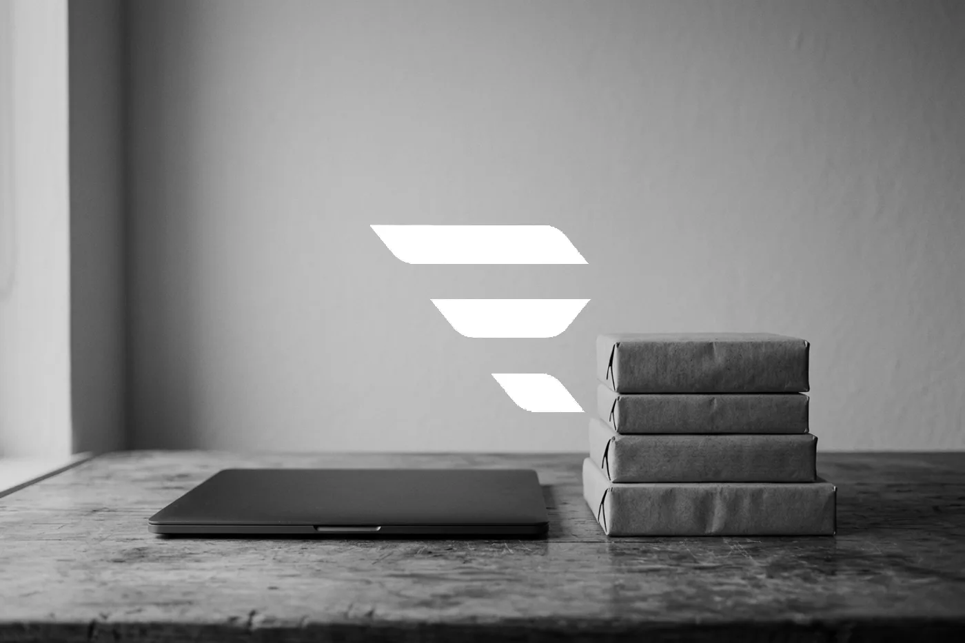 A closed laptop beside a stack of wrapped parcels on a wooden table